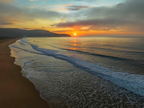 Peaceful sunrise over the ocean with small waves and clouds