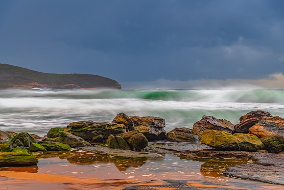 Sunrise at the seaside with rocks and rain clouds