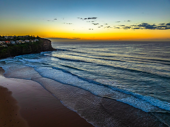 Sunrise at the beach with waves and a smattering of clouds