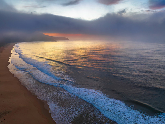 Peaceful sunrise over the ocean with small waves, clouds and fog