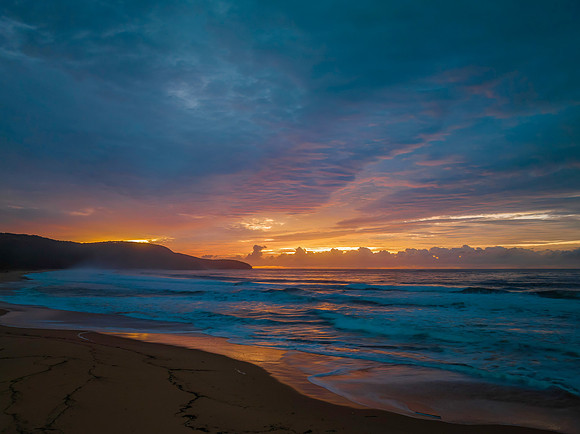 Cloud covered sunrise at the seaside in pink and blue
