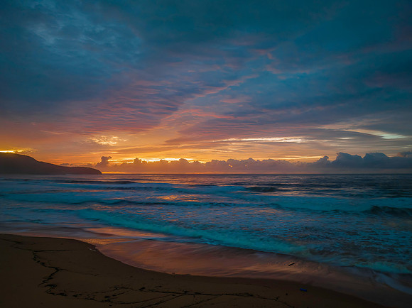 Cloud covered sunrise at the seaside in pink and blue
