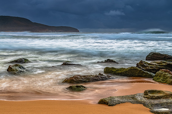 Sunrise at the seaside with rocks and rain clouds