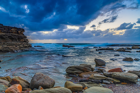 Moody sunrise seascape with clouds at the rocky inlet