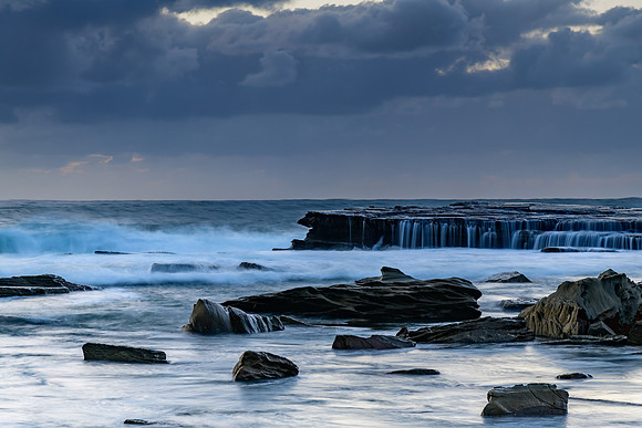 Moody sunrise seascape with clouds and casscades over the rock p