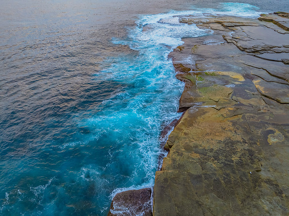 Sunrise and the blue sea washing over the rock platform
