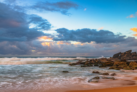 Sunrise at the seaside with rocks and rain clouds