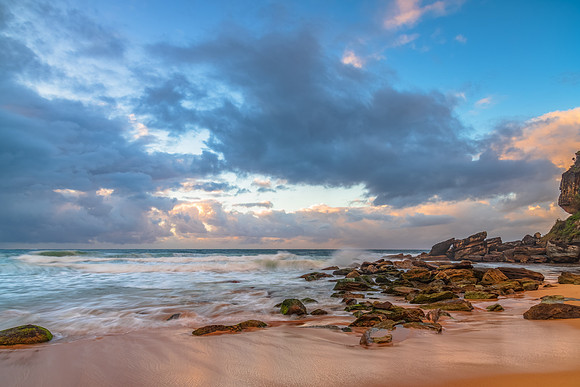Sunrise at the seaside with rocks and rain clouds