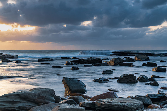 Moody sunrise seascape with clouds at the rocky inlet