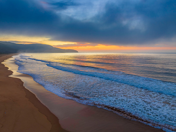 Peaceful sunrise over the ocean with small waves and clouds