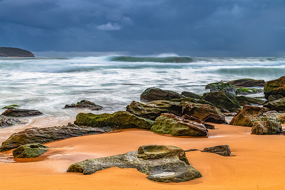 Sunrise at the seaside with rocks and rain clouds