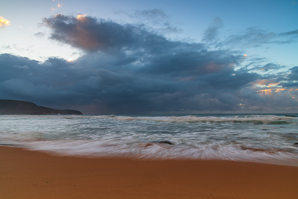 Sunrise at the seaside with rocks and rain clouds