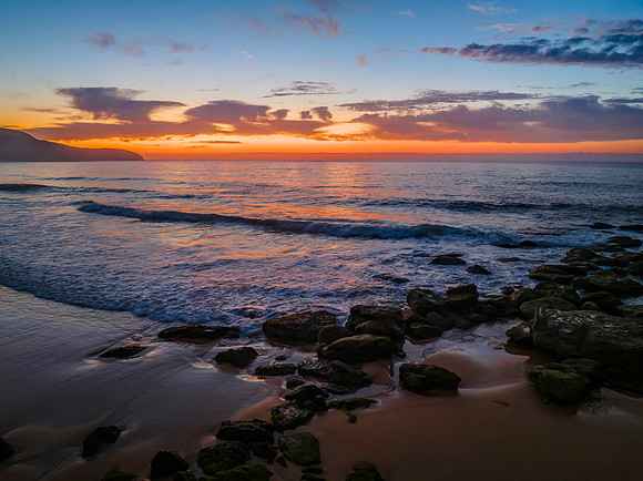 Orange dawn breaks over the ocean with small waves and clouds