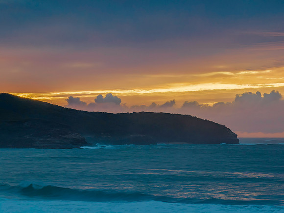 Cloud covered sunrise seascape and headland in soft pastel shade