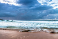 Sunrise at the seaside with rocks and rain clouds