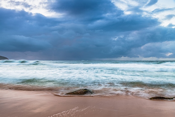 Sunrise at the seaside with rocks and rain clouds