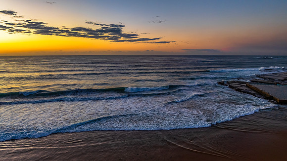Sunrise at the beach with waves and a smattering of clouds