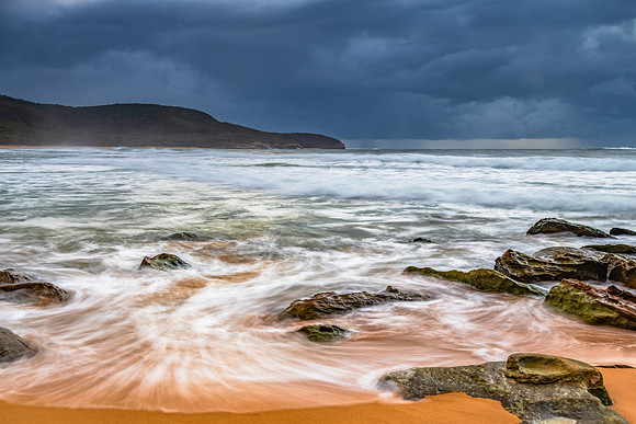 Sunrise at the seaside with rocks and rain clouds