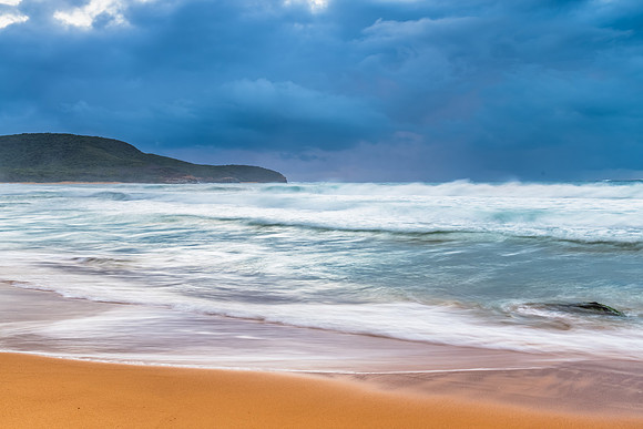 Sunrise at the seaside with rocks and rain clouds
