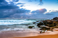 Sunrise at the seaside with rocks and rain clouds