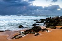 Sunrise at the seaside with rocks and rain clouds