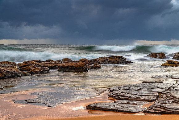Sunrise at the seaside with rocks and rain clouds