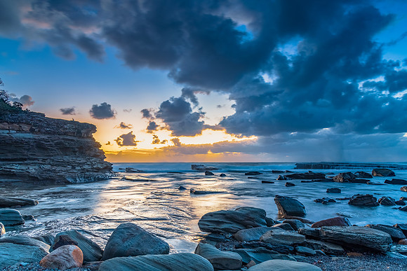 Moody sunrise seascape with clouds at the rocky inlet