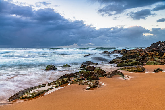 Sunrise at the seaside with rocks and rain clouds