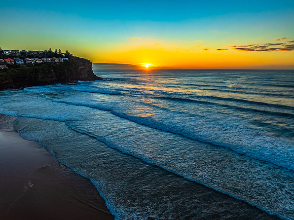 Sunrise at the beach with waves and a smattering of clouds