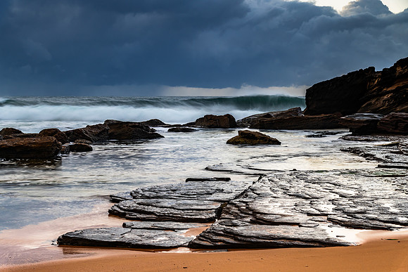 Sunrise at the seaside with rocks and rain clouds