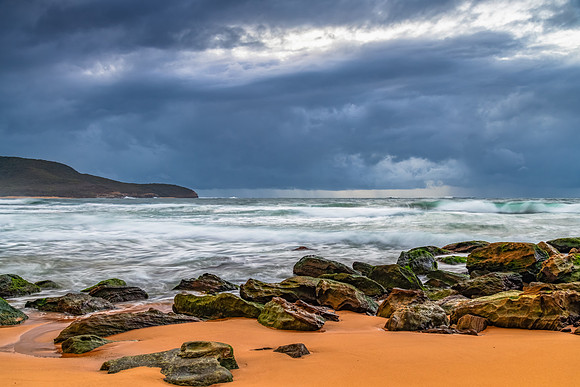 Sunrise at the seaside with rocks and rain clouds