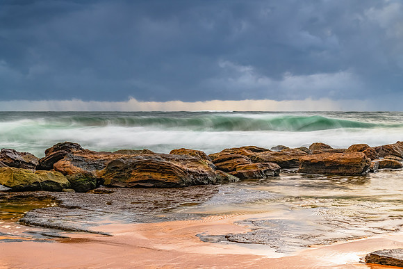 Sunrise at the seaside with rocks and rain clouds