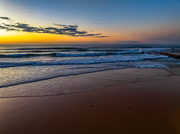 Sunrise at the beach with waves and a smattering of clouds