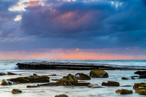 Moody sunrise seascape with clouds and casscades over the rock p