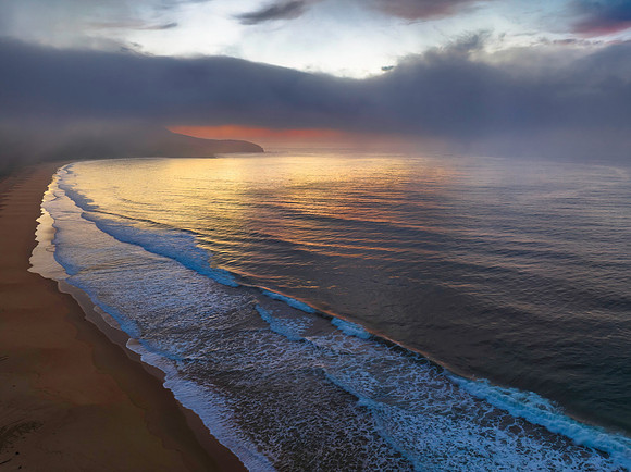 Peaceful sunrise over the ocean with small waves, clouds and fog