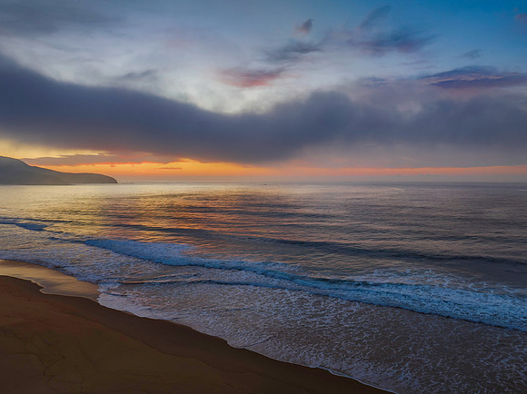 Peaceful sunrise over the ocean with small waves, clouds and fog
