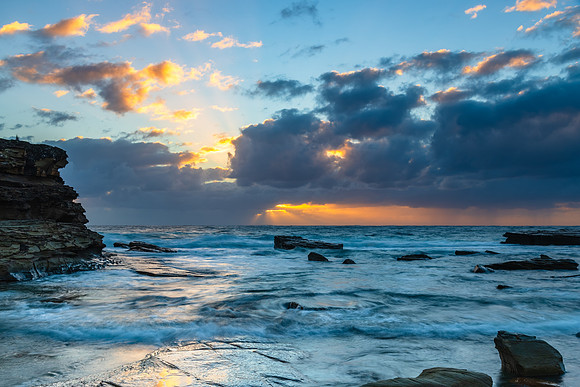 Moody sunrise seascape with clouds and sunrays at the rocky inle