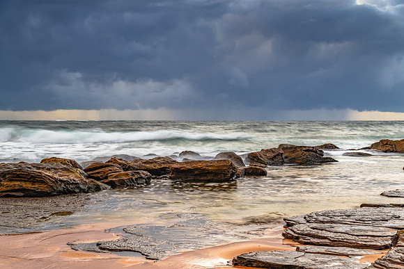 Sunrise at the seaside with rocks and rain clouds